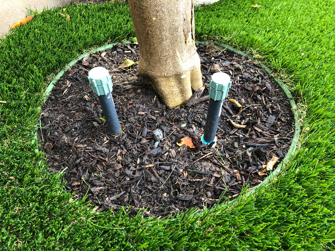 green artificial turf edging lining a tree well with black mulch