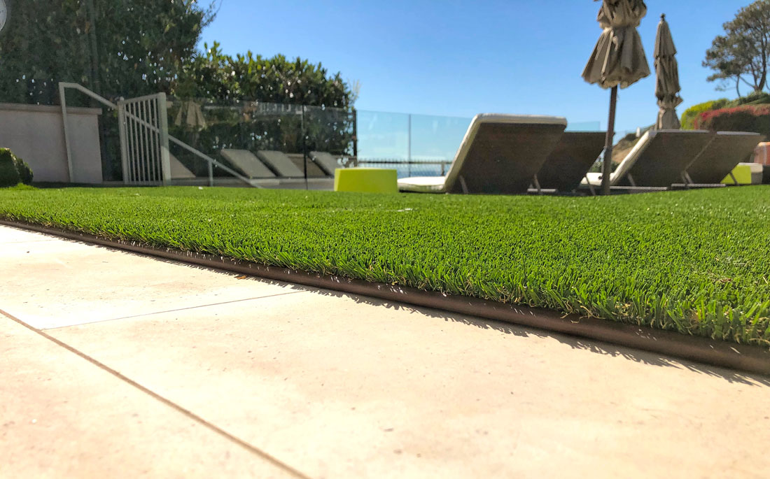 beige paving tile, brown artificial turf border, green artificial turf, lounging chairs by a pool